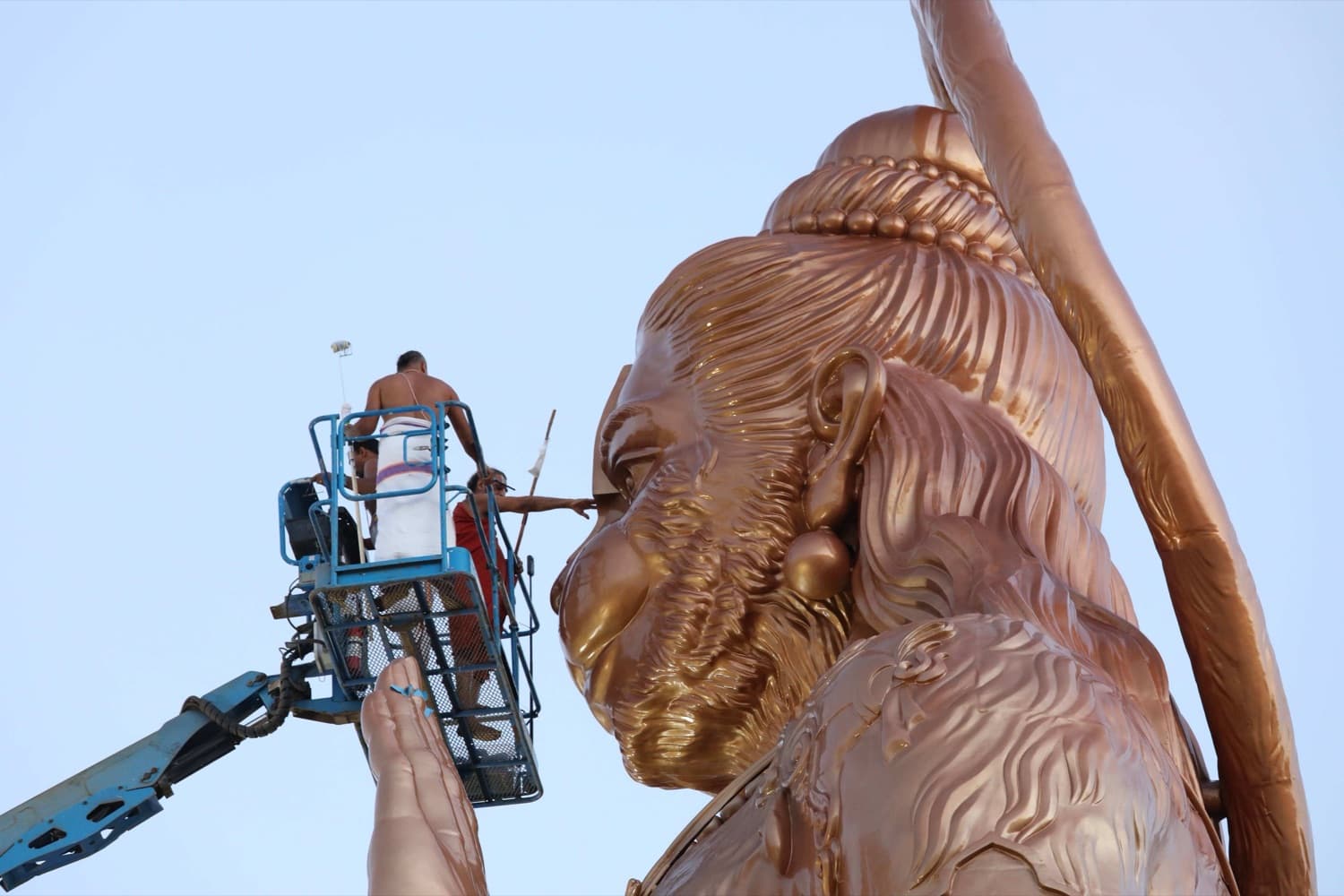 Artisans on a lift applying the gold finish to the face of the 90-foot Abhaya Hanuman statue